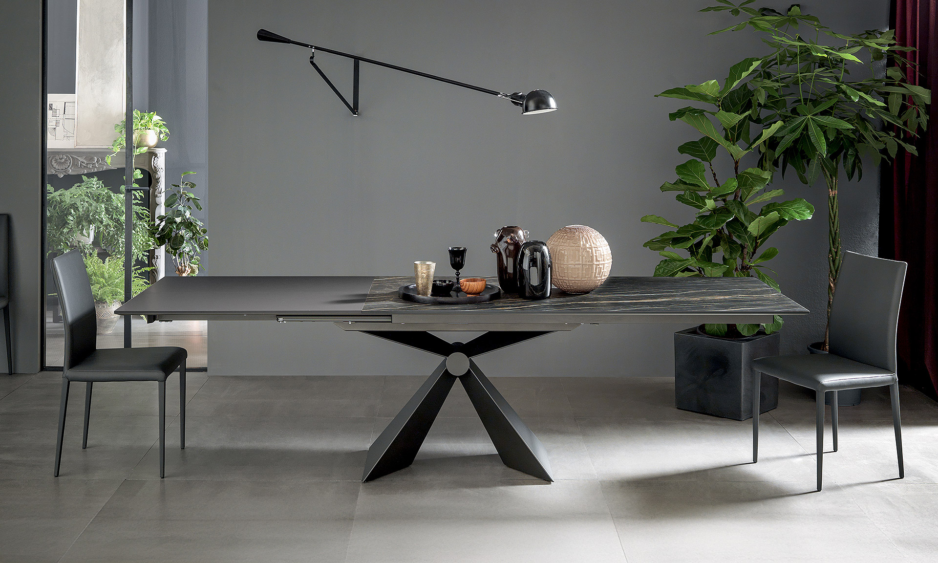 Photo d'une table avec rallonge intégrée. Pied central en V. Table avec plateau céramique noir veine blanche et rallonge gris anthracite.